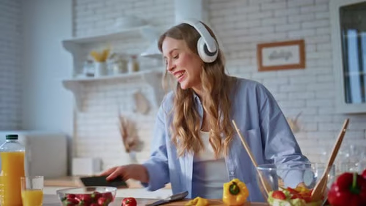 Mujer cocinando en casa con auriculares mientras sigue una preparación
